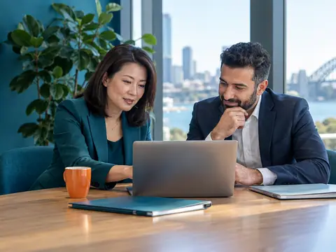 An accountant reviews a laptop with a client at a meeting table in a bright office with a teal wall and plant